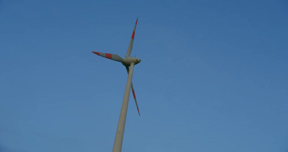 A wind turbine spins high in a clear blue sky
