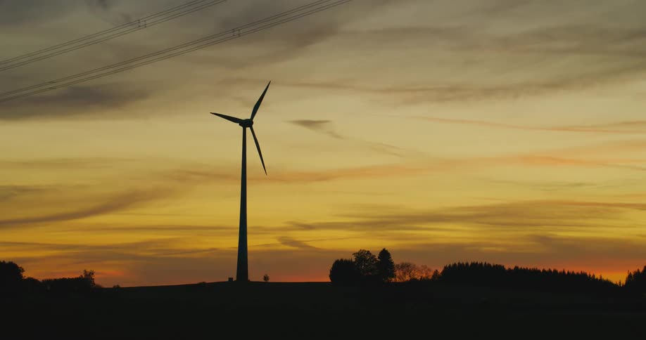 Silhouette of a wind turbine spinning on the countryside at evening