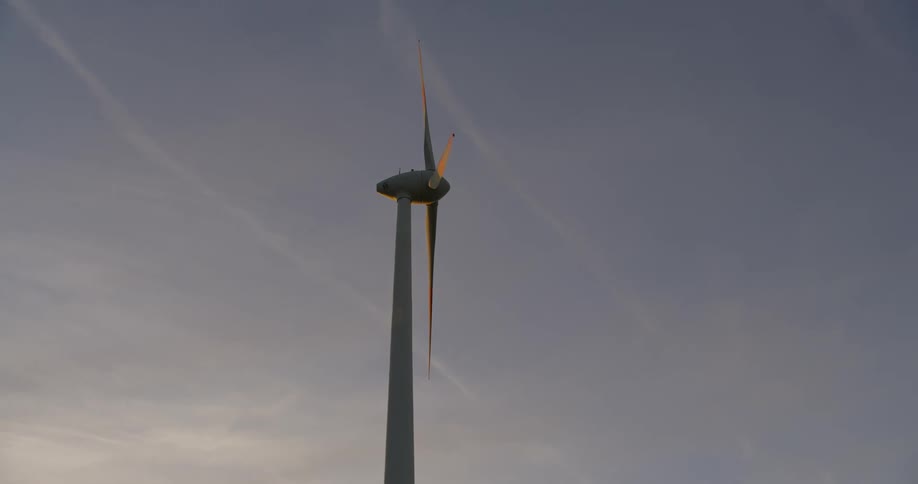 A rotating wind turbine in a field at sunset