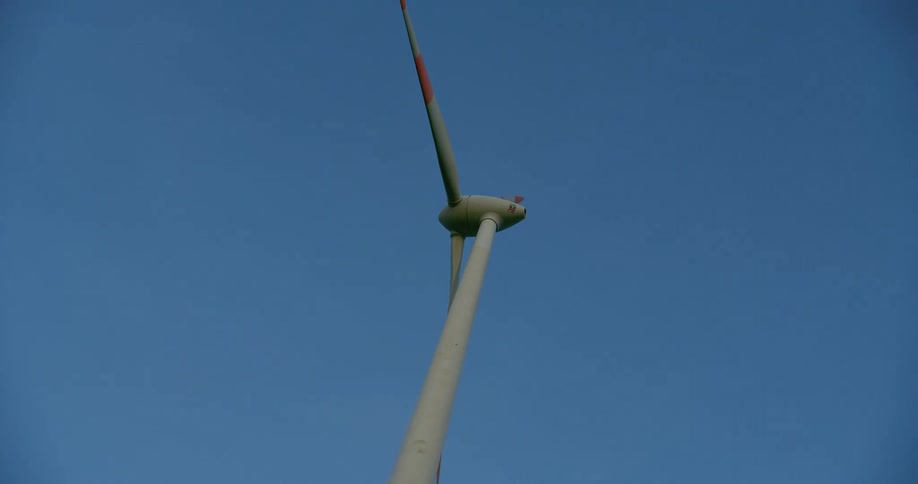 A wind turbine spins high in a clear blue sky