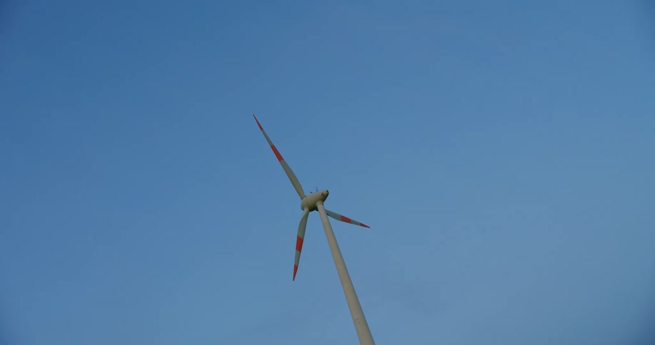 Wind turbine with striped blades stands under blue sky