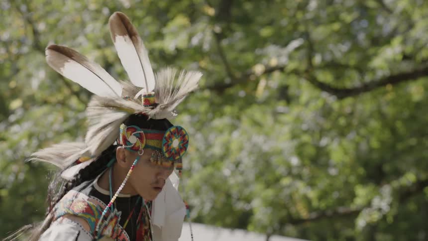 A man wearing a native american indian costume performs a dance