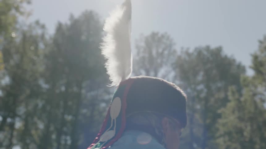 A man wearing native dress dances in bright sunlight