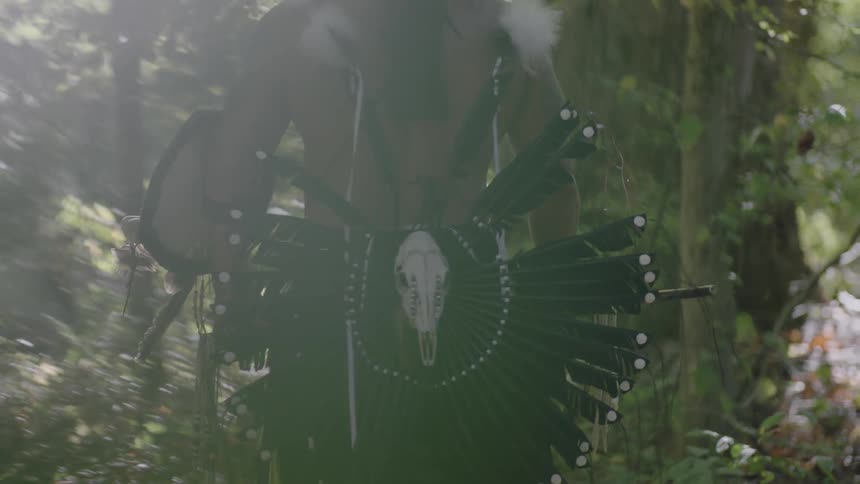 A man with feathers on something on his back, just standing in the woods