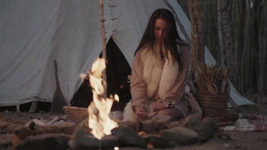 A woman kneels on the ground next to a burning fire