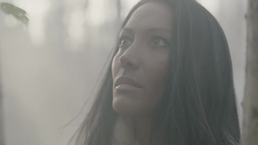 A woman standing in the woods as fog swirls around her