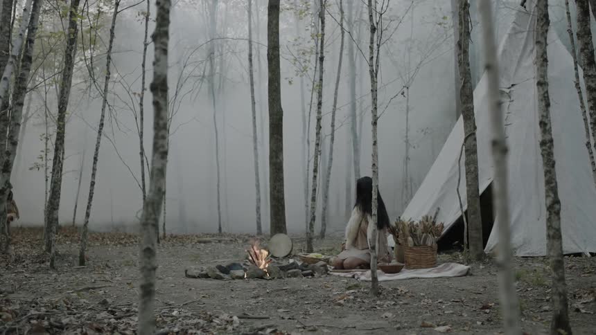 A woman and child outside a teepee by a campfire