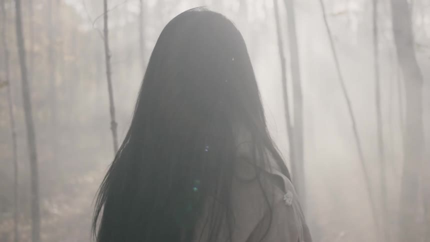 A woman looks around a foggy forest