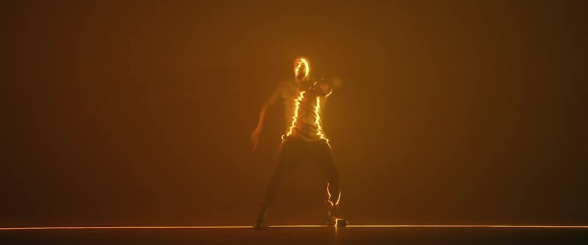 Male dancer performs routine while blending into amber background and being illuminated by amber light
