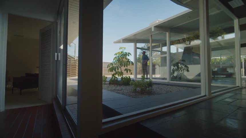 A man stands next to a floor to ceiling window at his home and takes in the view