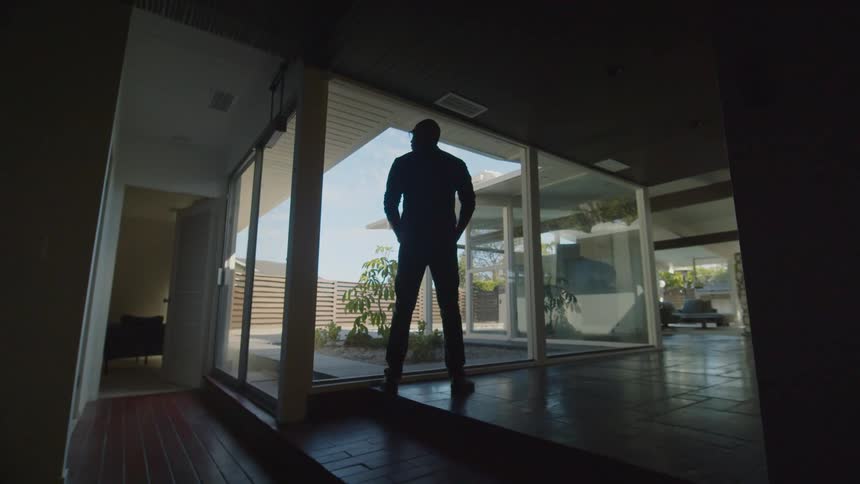 A tall male stands at a window that faces the courtyard of a residential home