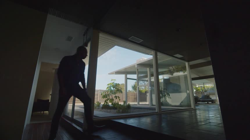 A man walks down a hallway in his house to look out the window