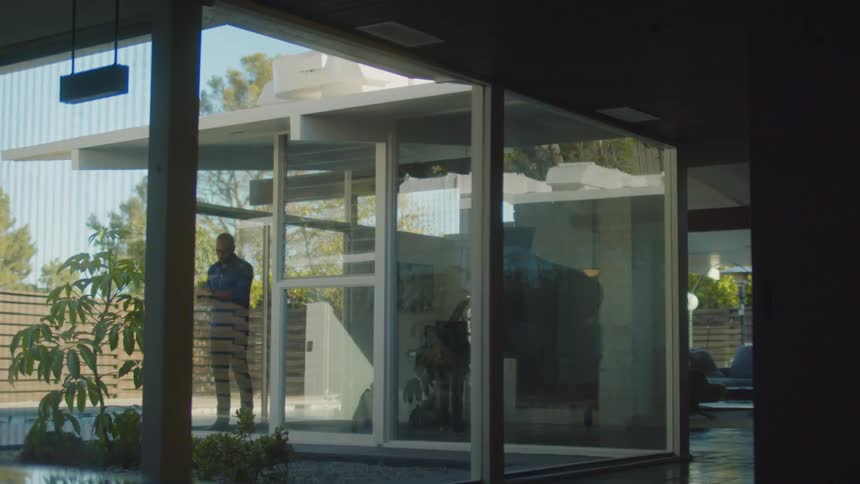 A man stands and looks around next to an open door of his residence leading to its yard