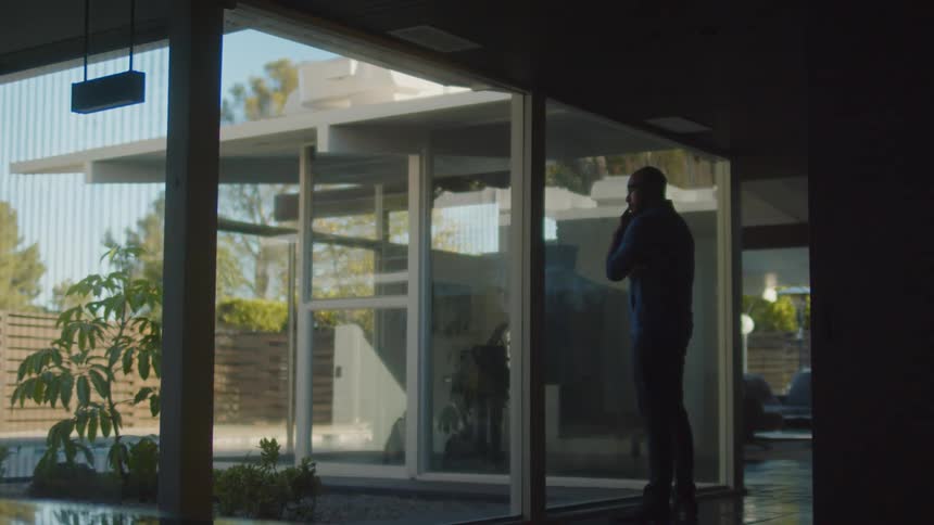 A man is standing indoors and looking out a window