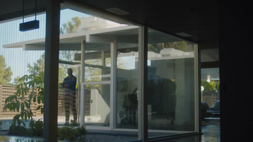 A man crosses his arms while looking out the window of his modern home