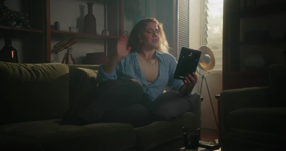 Woman sits on couch having video call via tablet