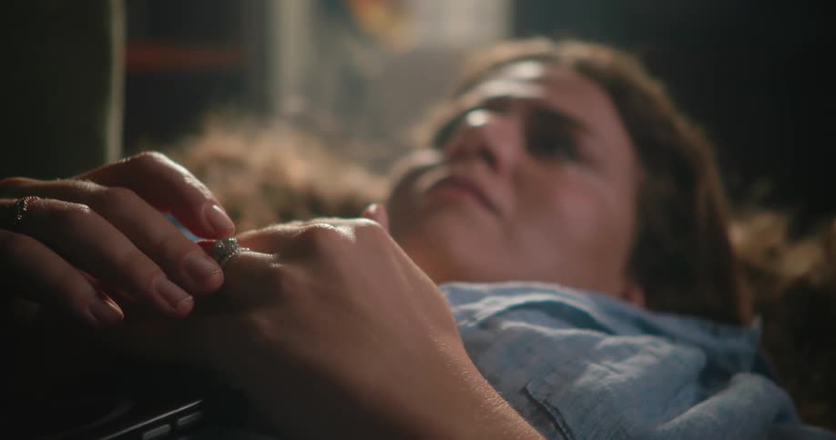 A woman lays on her back while looking upward as she mindlessly touches her ring