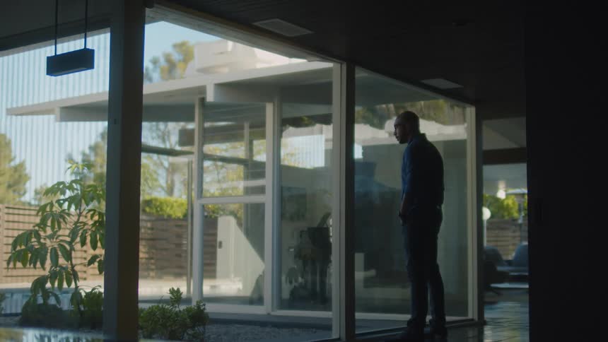 A man stands and looks out the window of his modern home