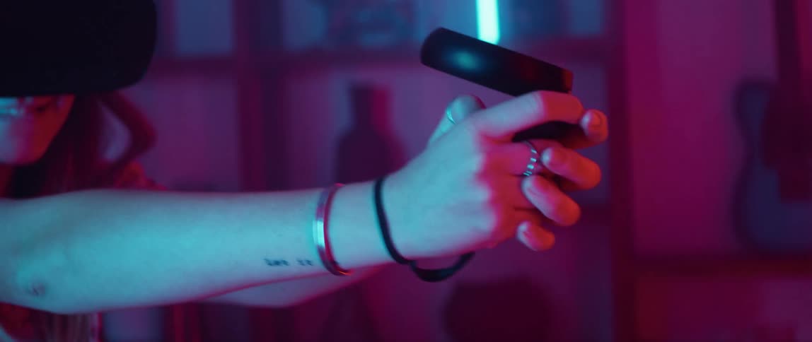 A teenage girl wearing a virtual reality headset and holding a controller is moving and turning around in a room illuminated with colored lights