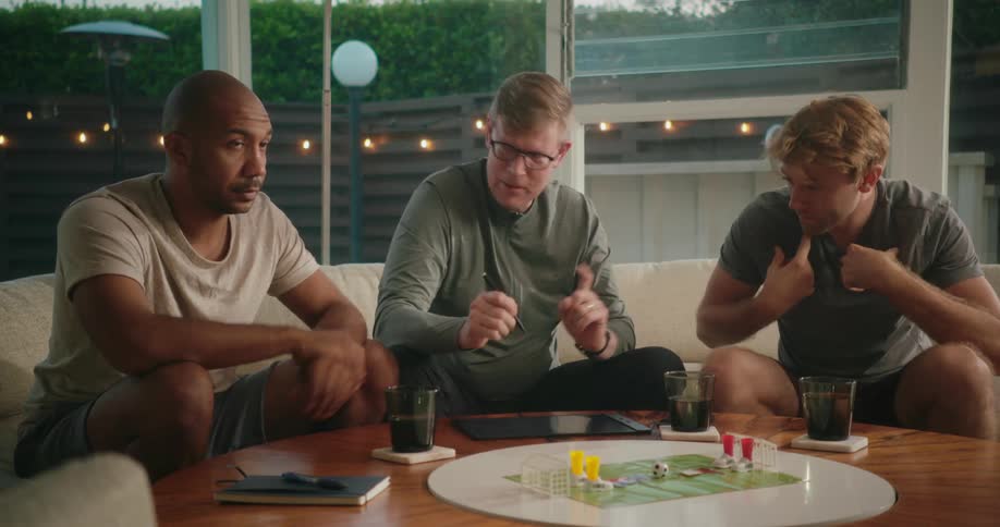 A group of men play a board game using a tablet