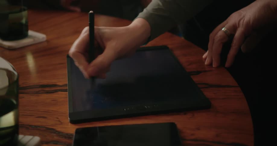 Two people viewing and writing on a tablet on a wood table