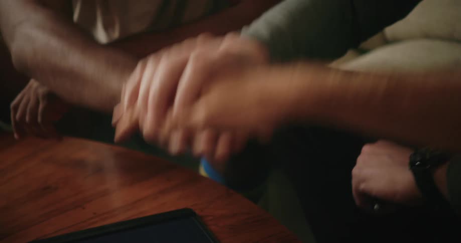 Three men sit on couch and stack their hands together