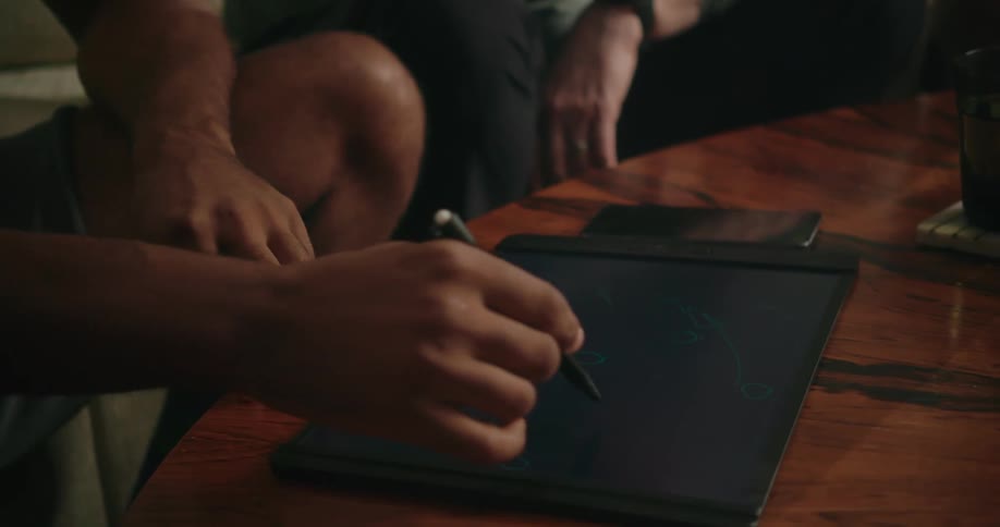 Man sketches on electric pad set on rotating table while conversing with another man