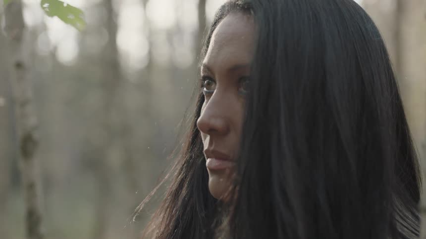A woman stands beside several tree trunks