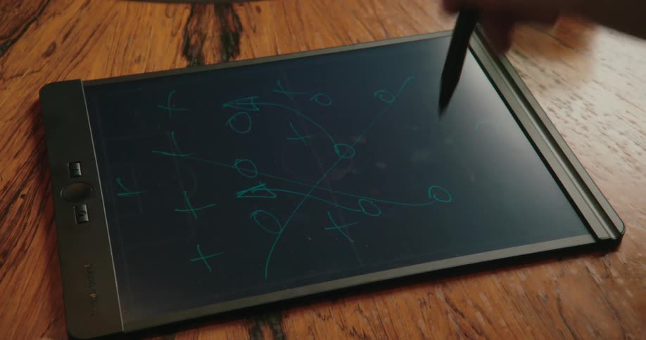 A person points at a tablet and a man uses a stylus to cross out the drawing on the tablet