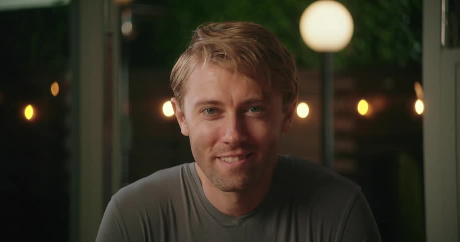 A man slowly looks upwards and then directly into the camera as he smiles