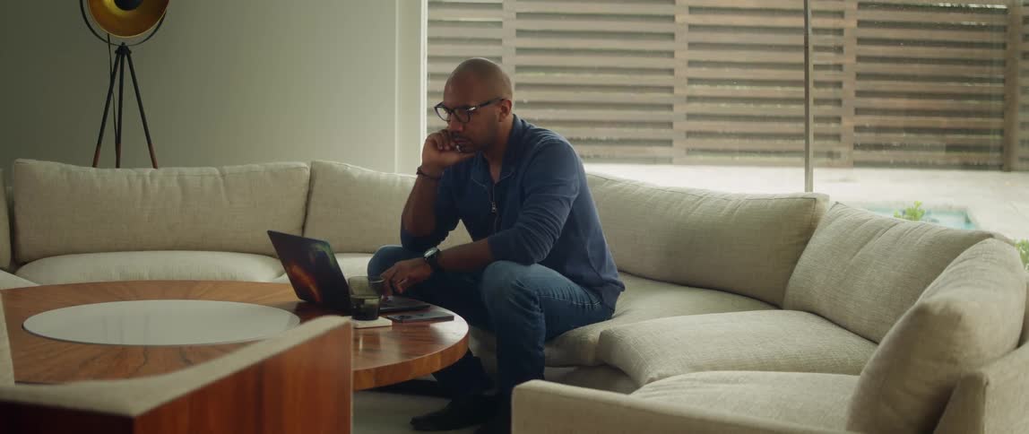 A man sits on a couch at home and looks at his laptop
