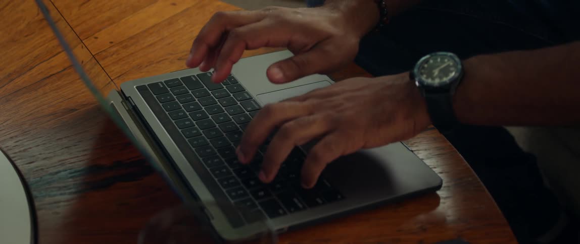 Close up of mans hands typing on laptop keyboard on coffee table in the living room