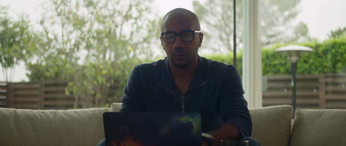 A man is sitting on a couch and typing on a laptop