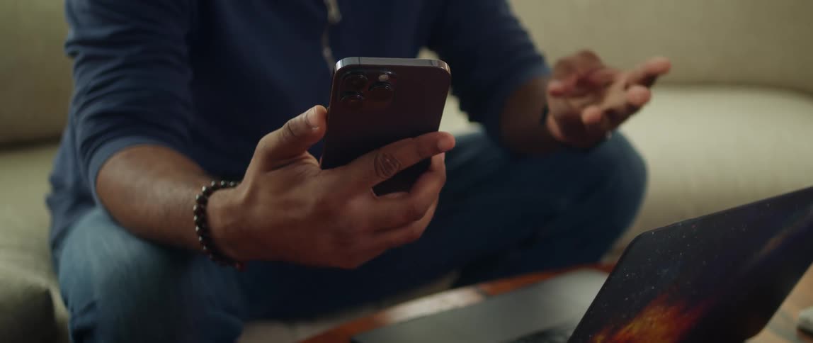 Man sitting on a couch in front of a laptop counts with his fingers while holding a smartphone