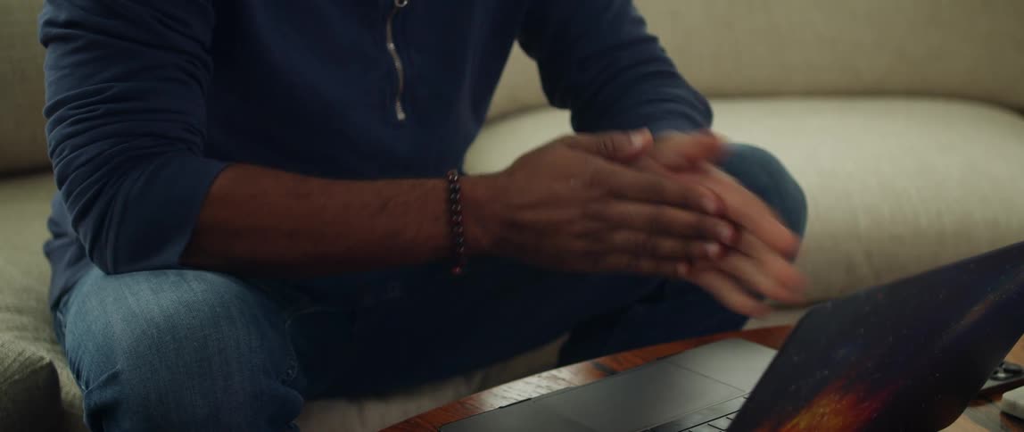 A man puts down his phone and rubs his hands together before typing on his laptop