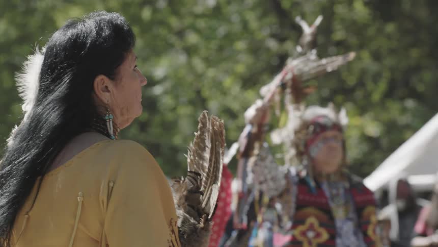 A woman carrying feathers on a sunny day in front of a crowd