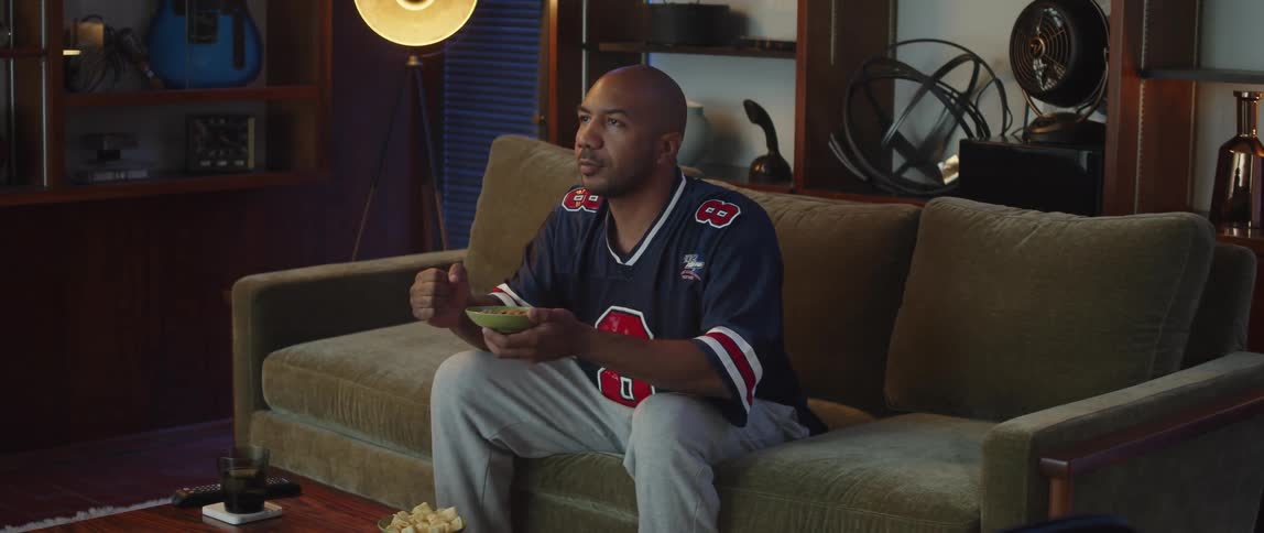Young man sitting on a couch at home watching sports celebrates excitedly while eating snacks