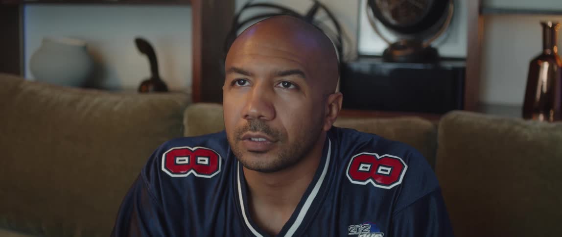 Man wearing sports jersey sits on couch snacking while watching television