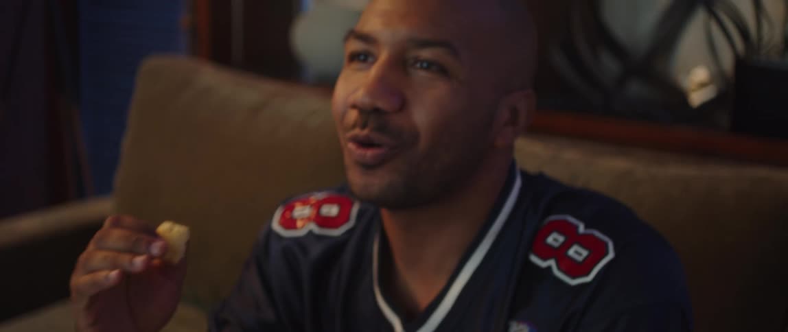 Young man sitting on a couch at home watching sports celebrates while eating popcorn