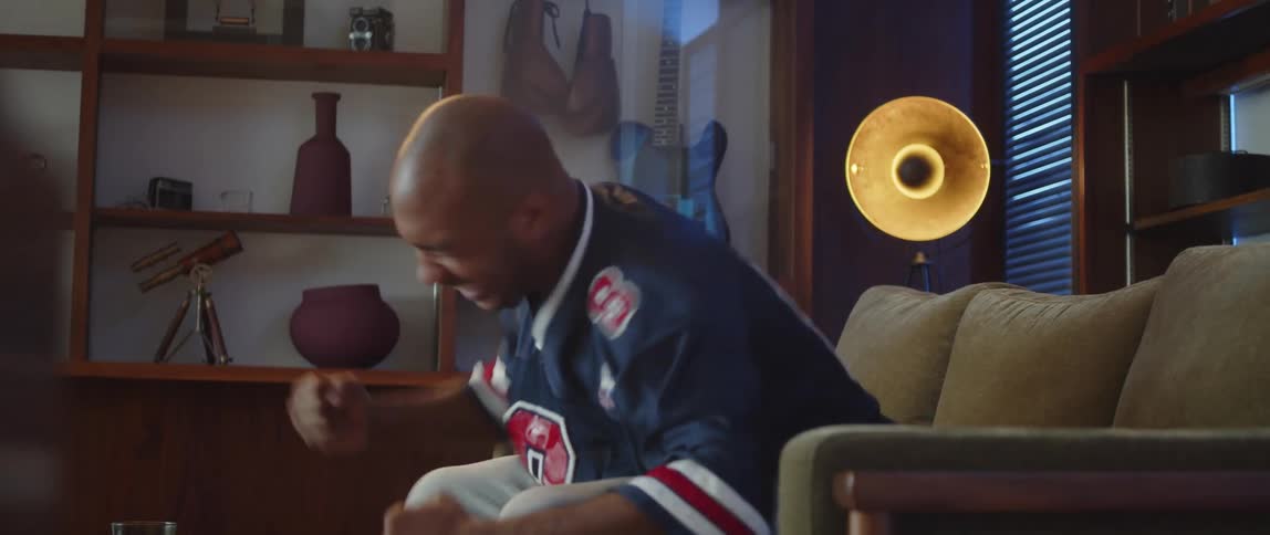 Young man sitting on a couch a home watching sports celebrates excitedly a good play