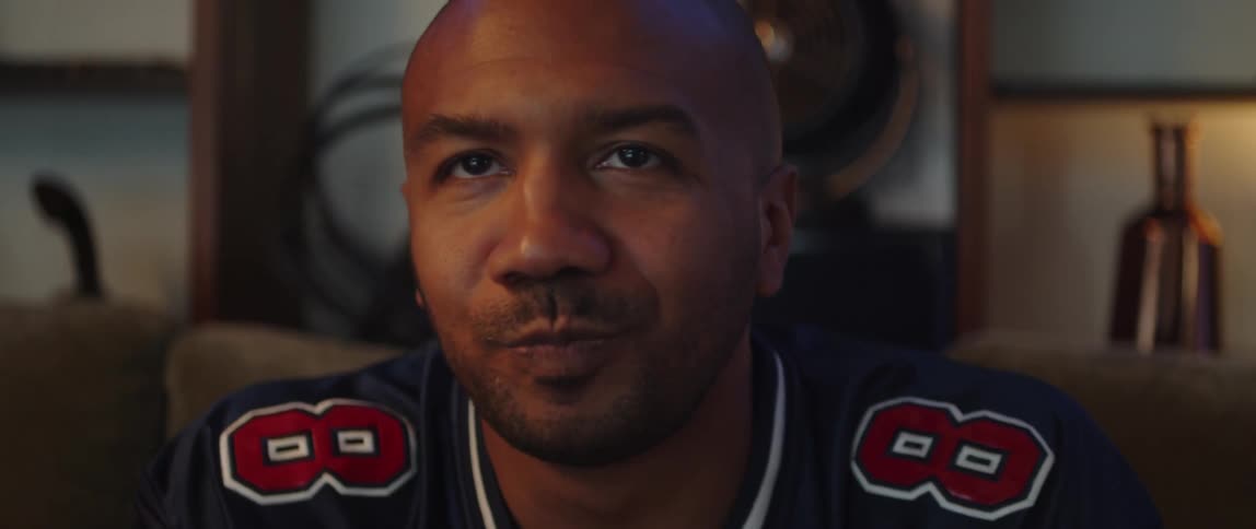 A man sitting on a couch watching sports eats a snack