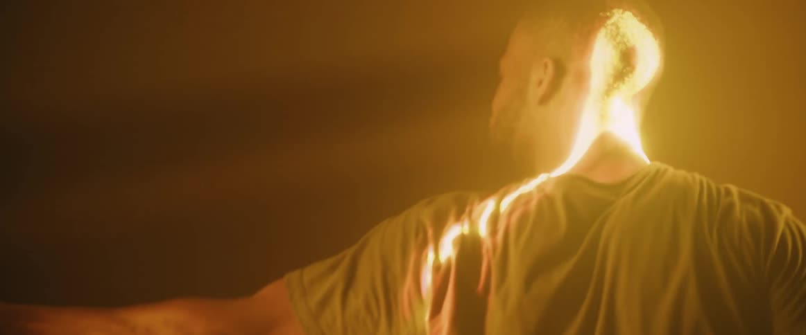 Male dancer performs against an amber background while his movements are highlighted by a projected beam of light