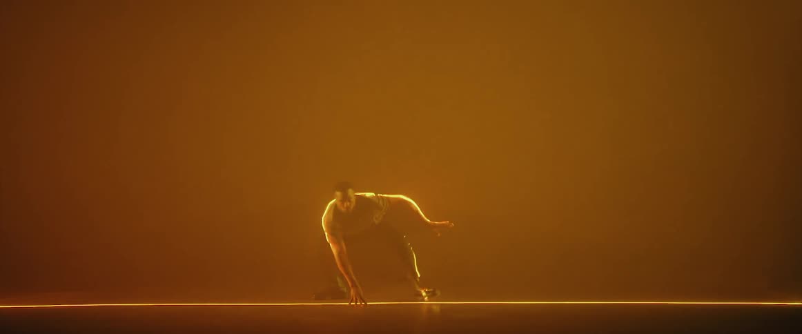 Artist performing dance moves on a stage behind a wall of light reflecting on white smoke