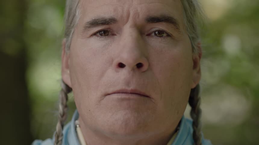 A man with braided hair looks up and toward the camera