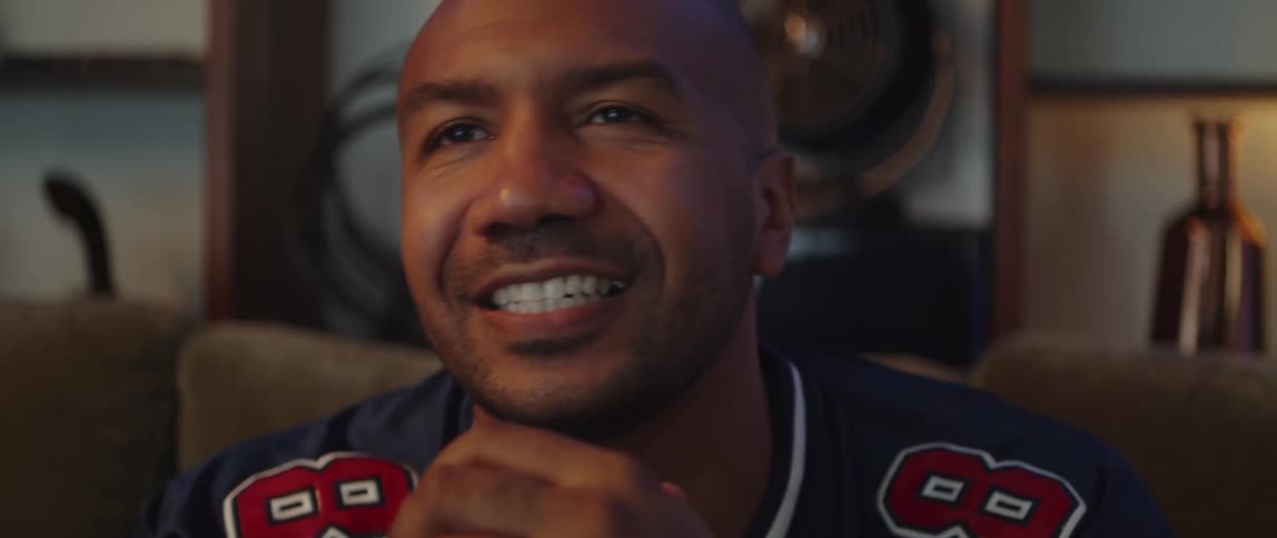 A man is sitting in anticipation with his hands folded in front of him and then he smiles and cheers clenching his fists in the air
