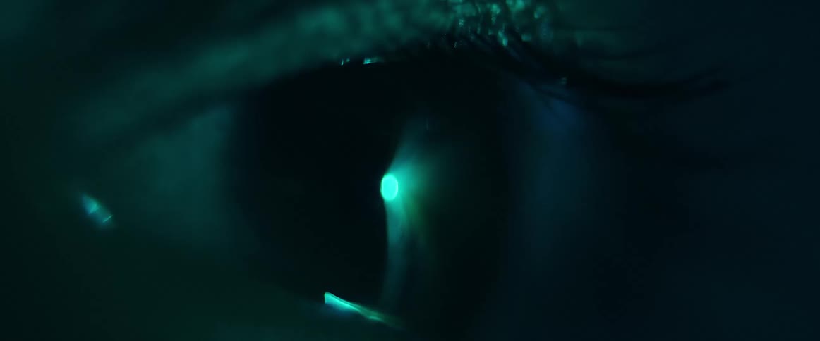 A human eye slowly opens and beams of light are seen reflecting in it