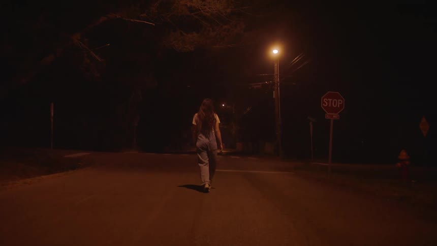 A woman walks down the middle of a neighborhood street at night