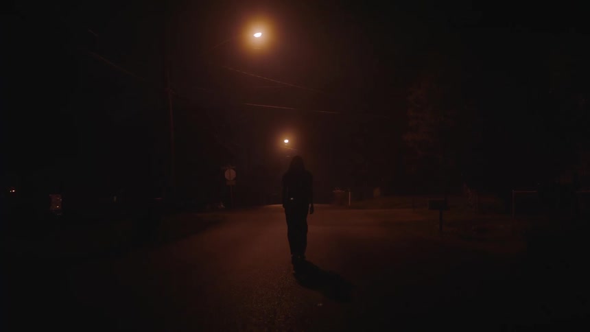 Silhouette of a woman walking on an empty town street under dim streetlights at night