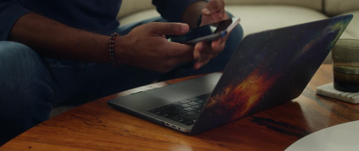 A man checks his smartphone while working on his laptop at home