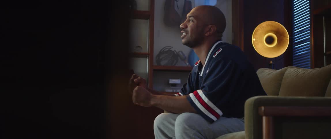 Man wearing a sports jersey sits on couch cheering while watching sports broadcast